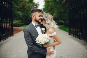 Mariés se tenant tendrement dans une allée pavée, bouquet de roses blanches à la main