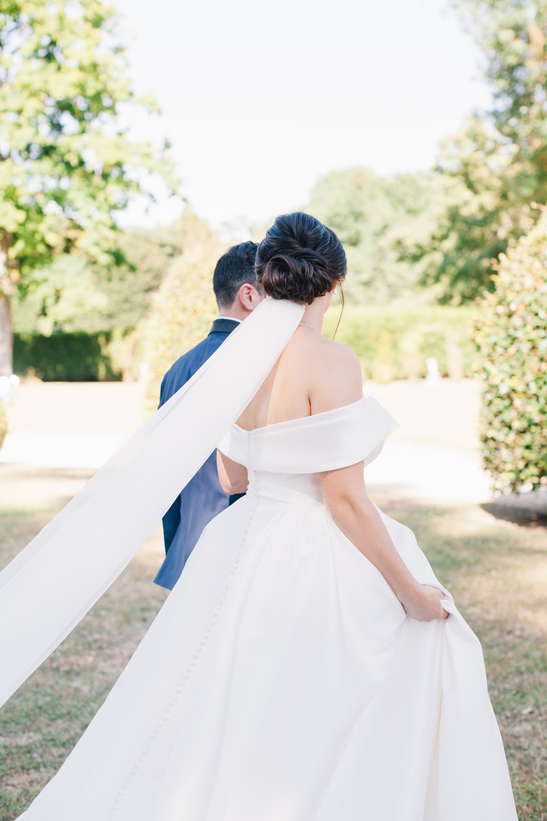 Mariée en robe blanche dos nu avançant main dans la main vers la cérémonie