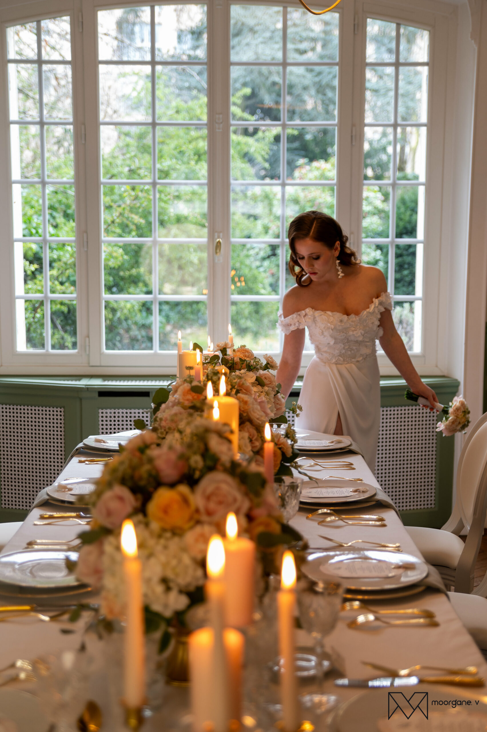 Mariée élégante observant une table de mariage ornée de bougies et fleurs pastel