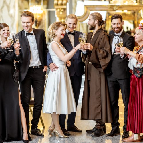 Large group of elegant people well-dressed in retro styles standing together with drinks at the luxury restaurant during the grand celebration