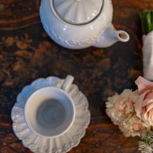 Petit bouquet de mariée posé à côté d’une tasse et théière en porcelaine blanche