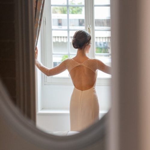 Mariée de dos ouvrant les rideaux, capturée à travers un miroir avant la cérémonie